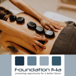 Lady lying on her front, with a brown towel around her waist, during a Hot Stones Therapy course, the therapist's hands are either side of stones lined down the spine