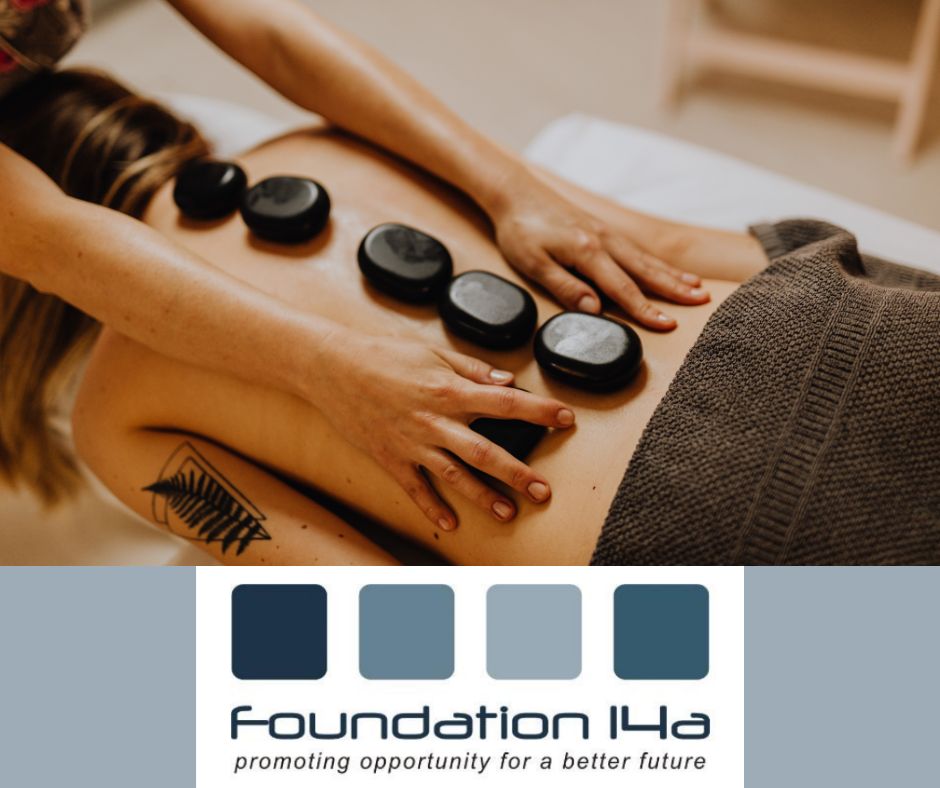Lady lying on her front, with a brown towel around her waist, during a Hot Stones Therapy course, the therapist's hands are either side of stones lined down the spine