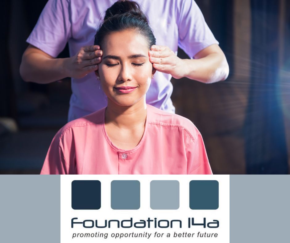 An Asian lady in a pink top sitting with her eyes closed facing the camera is being treated on the Indian Head Massage course by a therapist in a purple uniform behind her.