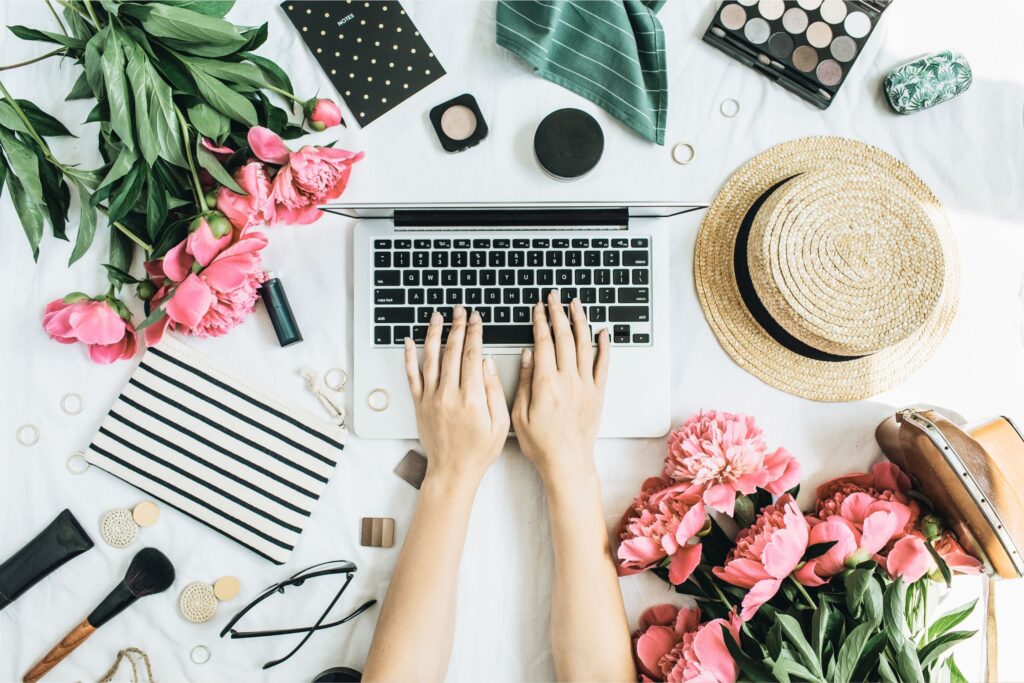 Beauty Blog being created on a laptop with a desk filled with pink flowers, a hat and makeup